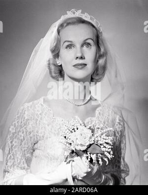 1950ER JAHRE PORTRÄT DER BLONDEN BRAUTDEMURE AUSDRUCK MIT SPITZE SCHLEIER HALTEN BRAUTBOUQUET - B2290 DEB001 HARS FRAUEN VERHEIRATETE STUDIO SHOT EVENT KOPIE RAUM FREUNDSCHAFT HALBE LÄNGE DAMEN EHE PERSONEN INSPIRATION FÜRSORGLICHE SCHLEIER SPIRITUALITÄT VERTRAUENSFEIER B&W BRAUTTRÄUME ABENTEUER BRÄUTE STILE TRADITION NUPTIALE NUPTIALS ANLASS HOCHZEIT STOLZ KONZEPTIONELL RITE OF PASSAGE STYLISH DEB001 STRANG WED STARRY EYED MODE LILY OF VALLEY MARRY MATRIMONY YOUNG ADULT WOMAN BLACK AND WHITE CAUCASIAN ETHNICITY DEMURE OLD FASHIONED Stockfoto