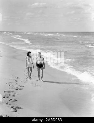 1930ER JAHRE VIERZIGER JAHRE PAAR MIT BADEANZÜGEN, DIE ZUSAMMEN GEHEN AUF EINER HELLEN, SONNIGEN KÜSTE MEER STRAND SAND - B7062 HAR001 HARS GESUNDE BALANCE STARKE FREUDE LEBENSSTIL OZEANZUFRIEDENHEIT FRAUEN EHEPARTNER EHEMÄNNER GESUNDHEIT KOPIE RAUM FREUNDSCHAFT VOLLE DAMEN PERSONEN SZENISCHE INSPIRATION FÜRSORGLICHE MÄNNER SONNENLICHT WARME GELASSENHEIT B&W PARTNER FREIHEIT AKTIVITÄT TRÄUME GLÜCK KÖRPERLICH HELL WELLNESS HOHER WINKEL FREIZEIT KRAFT ERHOLUNG AUF SCHLENDERN KONZEPTUELLE FLUCHT FLEXIBILITÄT MUSKELN SONNENBESCHIENENE BADEANZÜGE PERSÖNLICHE ANHÄNGLICHKEIT LIEBE EMOTIONEN MITTELERWACHSENE MAN-FRAU MITTLERER ERWACHSENER Stockfoto