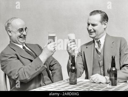 DREISSIGER JAHRE ZWEI MÄNNER FRÖHLICHE LÄCHELNDE GESCHÄFTSLEUTE SITZEN AM TISCH UND BEWUNDERNSWERTE BRILLE BIER LEERES DUNKLES GLAS FLASCHEN AUF DEM TISCH - F442 HAR001 HARS ALTE MODE 1 KOMMUNIKATION FLASCHEN FREUND TEAMARBEIT ENTSPANNUNG FREUDE LIFESTYLE ZUFRIEDENHEIT FEIER ÄLTERES STUDIO KOPIE RAUM FREUNDSCHAFT HALBE LÄNGE PERSONEN TISCHDECKEN MÄNNER ERHÖHEN VERTRAUEN SENIOR MAN WESTE SENIOR ERWACHSENE B&W ANZUG UND KRAWATTE VERKAUFEN GLÜCK ALTER OLDSTERS FRÖHLICHER OLDSTER GETRÄNK FREIZEIT FLÜSSIGER VATER UND SOHN AUF DEM LÄCHELN ÄLTESTE VERBINDUNG DREITEILIGER ANZUG FREUNDLICH FREUDIG AUFZIEHEN STILVOLLE BREWSKI-ZUSAMMENARBEIT Stockfoto