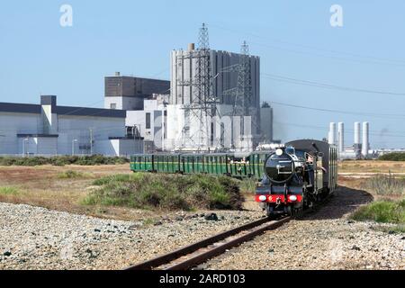 Ein Zug auf der schmalspurigen Romney, Hythe and Dymchurch Railway fährt östlich von Dungeness, im Hintergrund das Kernkraftwerk Dungeness B. Stockfoto