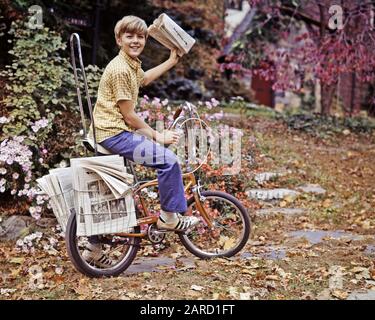 1970ER JAHRE NEWSBOY AUF DEM FAHRRAD AUF DER VORORTSTRASSE MIT ZEITUNG BEREIT ZUR LIEFERUNG - KJ5027 PHT001 HARS BEREIT FAHRRADFAHREN NATUR FÜRSORGLICH MÄNNER TURNSCHUHE FAHRRÄDER DENIM FAHRRÄDER ZIELE TRÄUME FRÖHLICHE HERBST SAISON ARBEIT STOLZ CHANCE BESCHÄFTIGUNG LÄCHELN VERBINDUNG GEBEN FREUDIGE UNTERSTÜTZUNG NEWSBOY MITARBEITER BLUE JEANS WACHSTUM LENKER JUGENDLICHE VOR TEENAGER VOR TEENAGER JUNGE WERFEN HERBSTLICHE KAUKASISCHE ETHNIE FALLEN LAUB MIT ALTMODISCHEN ARBEITEN Stockfoto