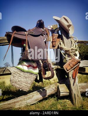 1960ER JAHRE 1970ER JAHRE WESTERN SADDLE COWBOY HAT SEIL LEDER PISTOLEN GÜRTELHOLSTER UND PISTOLEN HÄNGEN AN HOLZZAUN - KS9054 PHT001 HARS SIX GUN FIREARM FIREARMS FIREARMS RÜHRTE OLD FASHIONED Stockfoto