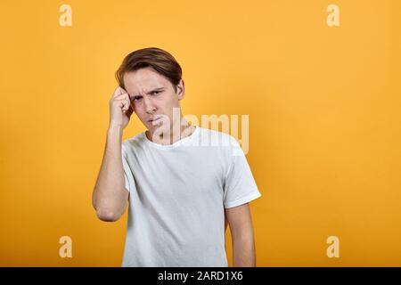 Der junge Mann hält seine Hand am Kopf und macht sich vor Kopfschmerzen ein Gesicht Stockfoto