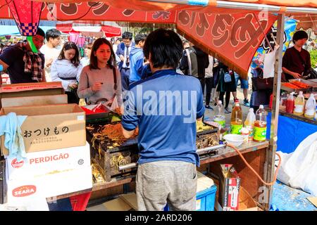 Über der Schulter des Stall Holers, der eine Plastikbox mit heißen Nudeln an junge Frau verkauft, mit vielen anderen Schlange hinter dem Osaka Castle Park, Japan. Stockfoto