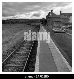 Schwarz-weiß [monochrom] eines einsamen Bahnhofs von Borth verschwinden die Gleise bis zum Horizont. Atmosphärische Wolken und ein traditioneller weißer Rahmen Stockfoto