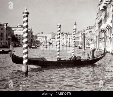 1950ER JAHRE ANONYMER GESCHÄFTSMANN, DER IM GONDELRUDERBOOT AUF DEM CANAL GRANDE DIE RIALTO-BRÜCKE IM HINTERGRUND VENEDIG ITALIEN FÄHRT - R7237 HAR001 HARS MÄNNER TRANSPORT B&W ERFOLG WEITWINKEL-SKILL-ANZUG UND KRAWATTE BERUF VERKAUFEN FÄHIGKEITEN ABENTEUER KUNDENSERVICE ITALIEN VENEDIG IN DEN BESETZUNGEN KONZEPTIONELL STILVOLL ANONYM MITTELADULTER MITTELERWACHSENER MAN-VERKÄUFER LÖSUNGEN SCHWARZ-WEISS-KAUKASISCHE ETHNIE HAR001 ALTMODISCH Stockfoto