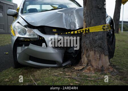 Silbernes, auf dem Sedan montiertes Straßenpflaster stürzte Kopf auf ein umwickeltes Warnband mit Baumgelb, Auckland, Neuseeland. Stockfoto