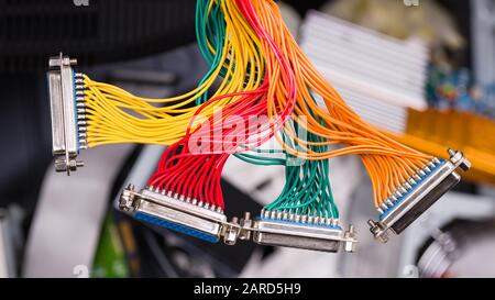 Farbige Kabelbündel, die lose über den Details der elektronischen Abfallentsorgung hängen. 25-polige Metallsteckverbinder. Isolierte Drähte an ausrangierten Computer- oder Laptop-Teilen. Stockfoto