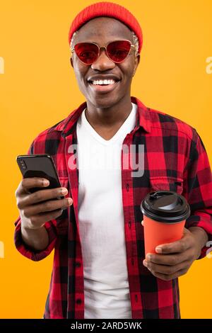 Porträt eines süßen schwarzen amerikaners, der stilvoll ein Getränkeglas auf einer Kaffeepause mit einem gelb hinterlegten Telefon-Hintergrund hält. Stockfoto