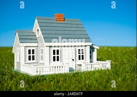 Miniaturhaus mit weißem Pickelzaun, der in einem grünen Rasen vor einem blauen Himmelshorizont steht Stockfoto