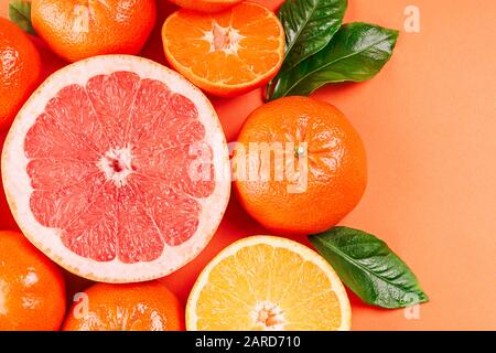 Frische reife Mandarinen, Grapefruit und Orangen mit grünen Blättern auf orangefarbenem Hintergrund. Stockfoto