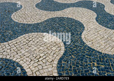 Traditionelles Kopfsteinpflaster in Portugal, schwarze und weiße Kopfsteinpflaster, die ein Wellendesign in Steinen bilden. Stockfoto