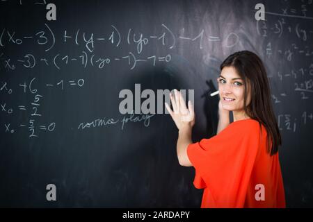 Hübscher, junger Student/junger Lehrer, der während eines Mathematikkurses auf dem Schwarzen Brett/an der Tafel schreibt Stockfoto