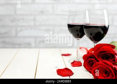 Valentinstag Stillleben. Zwei Gläser Wein, Rosenblätter und rote Rosen auf einem weißen Holztisch mit Platz für Text. Selektiver Fokus. Stockfoto