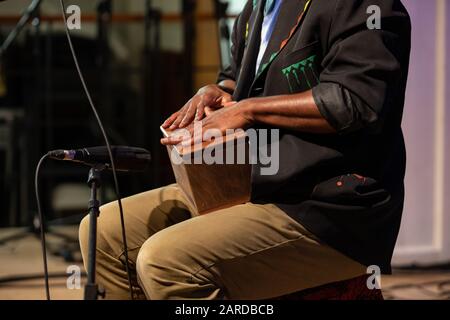 Mittelteil des afrikaners, der schwarzen Blazer trägt und während des Wettbewerbs Musik auf Holzkiste vor dem Mikrofon auf der Bühne spielt Stockfoto