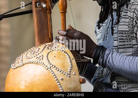 Mittelteil des männlichen Künstlers mit Dreadlocks, die Armbänder tragen und während der Veranstaltung traditionelle Holzharfenkora mit Fokus auf den Vordergrund ausführen Stockfoto