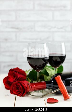 Valentinstag Konzept. Rote Rosen, Holzherz, Weinflasche, Korkenzieher und Gläser Wein auf Holz-Tafel. Stockfoto