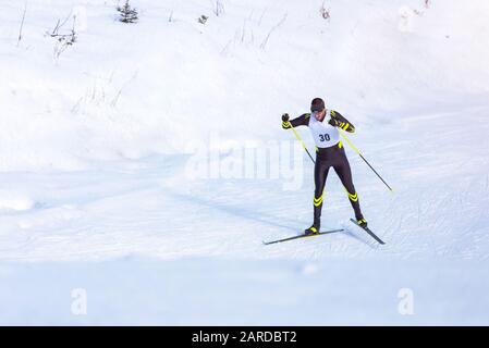 Ein Mann Skilangläufer auf der Strecke. Kerl mit moderner Skiausrüstung und Rennnummer Stockfoto