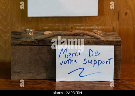 Nahaufnahme der geschlossenen Holzkiste mit "Danke für Ihre Unterstützung"-Text in französischer sprache mit blauer Tinte auf weißer Karte über strukturiertem Holztisch Stockfoto