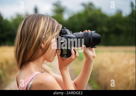 Profilansicht der jungen Frau, die in schöner Natur steht aufnehmen eines Fotos mit einer schwarzen dslr-Kamera, die das Bild fokussiert. Stockfoto