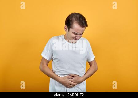Magenschmerzen Magenprobleme weißes T-Shirt junger Mann auf gelbem Hintergrund. Stockfoto