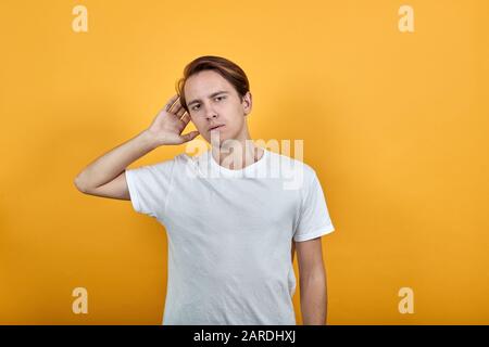 Mann in einem weißen T-Shirt, der Informationsklatsch auf gelbem Hintergrund ablauscht Stockfoto