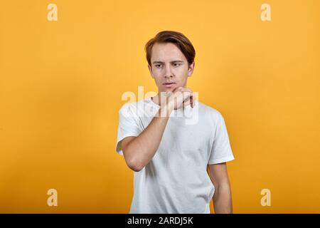 Gutaussehender junger Mann denkt, sein Kinn mit der Hand in einem weißen T-Shirt zu treiben Stockfoto