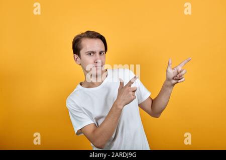 Ein gutaussehender junger Mann zeigt mit den Fingern in weißem T-Shirt die Richtung Stockfoto