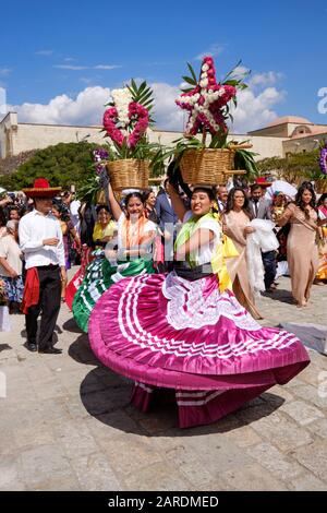 Frau tanzt in fließenden traditionellen Outfit mit Blumenkorb Teil der traditionellen Paradiese die Straßen von Oaxaca. Stockfoto