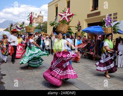 Frau tanzt in fließenden traditionellen Outfit mit Blumenkorb Teil der traditionellen Parade auf den Straßen von Oaxaca. Stockfoto