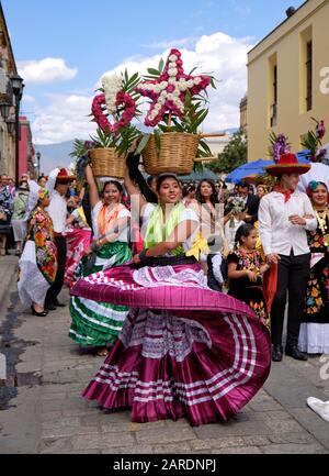 Frau tanzt in fließenden traditionellen Outfit mit Blumenkorb Teil der traditionellen Parade (Calenda de Bodas) auf den Straßen von Oaxaca. Stockfoto