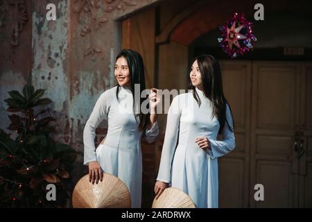 Zwei schöne Frauen, die Ao Dai vietnamesisches traditionelles Kleid tragen und Touristen zusammen im Stil des alten Hauses Frankreich Stockfoto