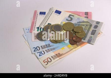 Viele Euromünzen und Cent auf ein paar Banknoten von zwanzig bis fünfzig Euro isoliert auf einem leeren Tisch Stockfoto