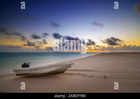 Kleines Dingy mit Außenbordmotor am Strand bei Sonnenuntergang Stockfoto