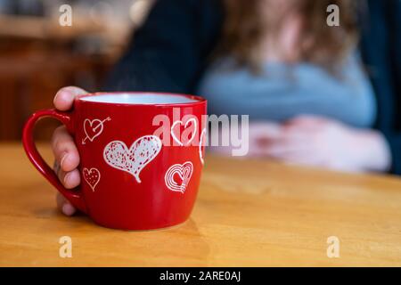 Ein selektiver Fokusschuss einer stark schwangeren Frau, die morgens in einem neuen roten Becher mit Herzen zubereiten kann, Valentines Morgengetränk mit Kopierraum Stockfoto