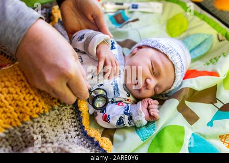 Ein Nahschuss an den Händen des Hausarztes, der die Gesundheit des süßen Jungen mit einem Traktor gemusterten Römer-Anzug überprüft und auf gesunden Herzschlag hört Stockfoto