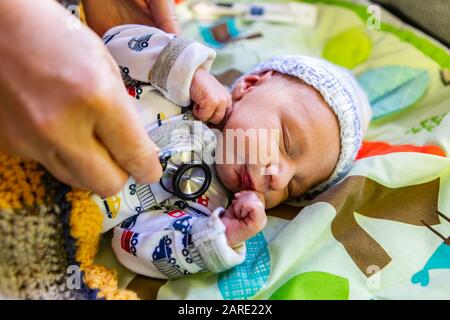 Erste Gesundheitskontrollen des neugeborenen Jungen, der in der Nähe als Geburtshelfer gesehen wird, verwenden Stethoskop, um die Gesundheit des tagelang alten Säuglings in bunten Decken zu überwachen Stockfoto