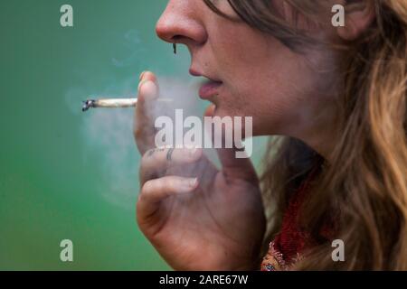 Closeup 3/4-Schuss aus der unteren Hälfte des Gesichts der kaukasischen Frau rauchend Hand gerollte Marihuana-Gelenke. Cannabisrauch wird von durchbohrter und tätowierte Frau ausgeatmet. Stockfoto