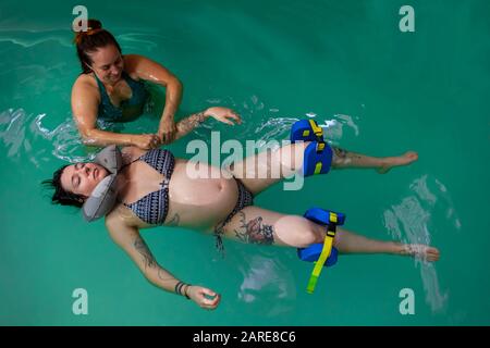 Hochwinkeliger Blick auf eine entspannte schwangere Frau mit Gummihalskissen um den Hals und Wassermassage im Schwimmbad mit Therapeut Stockfoto