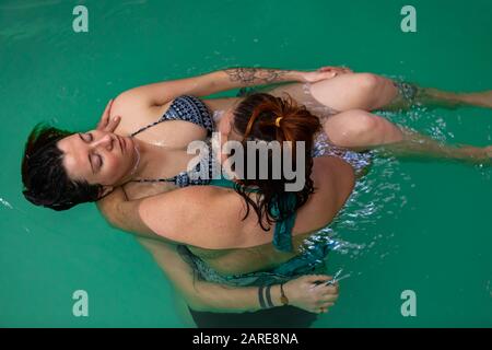 Entspannte schwangere Frau, die auf der Hand der Therpisten liegt, während sie sich im Schwimmbad befindet, um während der Schwangerschaft gesundheitlich behandelt zu werden Stockfoto