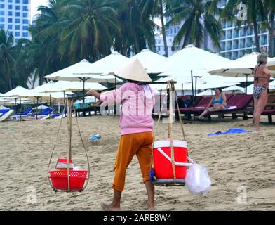 Ein Getränkehandelseller trägt zwei Container auf einem Schulterpol entlang des Strandes in Nha Trang in Vietnam, Asien, Südostasien. Stockfoto