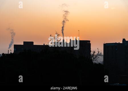 Urbane Landschaft mit der Silhouette von Gebäuden mit Kaminen, die Rauch bei Sonnenuntergang im Winter ausstoßen Stockfoto