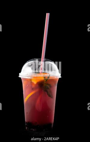 Frischer Cocktail mit wilden Beeren und Orange. In einem Glas Wildbeeren, orangefarbenen Scheiben, Minzblättern und Eiswürfeln. In den Tassen gibt es ein Trinkhalm. Isoliert auf schwarzem Hintergrund. Stockfoto