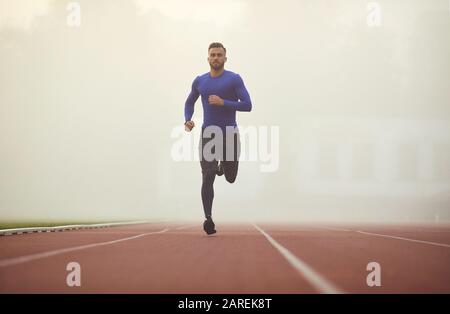 Ein junger Athlet läuft auf ein Stadion im Nebel. Stockfoto