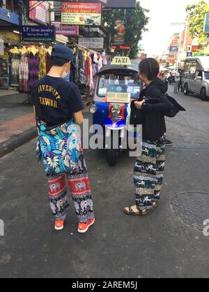 Bangkok, Thailand. Januar 2020. Touristen stehen auf einer Straße in Thailands Hauptstadt Bangkok in sogenannten Elefantenhosen vor einem Tuk-Tuk, einem offenen Autorrickshaw. Die breite, luftige Hose mit wilden Elefantenmustern ist bei Touristen in Südostasien beliebt. (Zur dpa "Warum tragen Touristen Elefantenhosen?") Credit: Caroline Bock / dpa / Alamy Live News Stockfoto