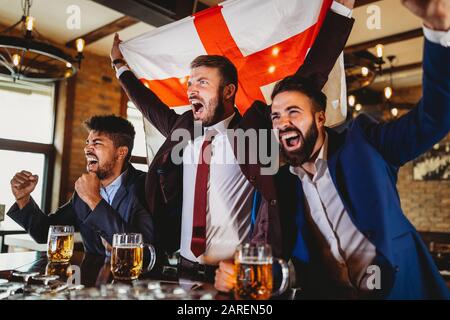 Männerfans schreien und beobachten Fußball im Fernsehen und trinken Bier in einer Kneipe Stockfoto