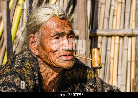 Porträt eines alten Apatani-Mannes, der die traditionelle Frisur mit dem Knop an der Stirn trägt, rauchende Pfeife Stockfoto