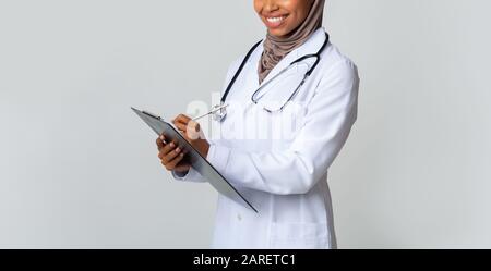 Black Muslim Medical Intern Girl In Hijab Schreibt Notizen An Clipboard Stockfoto