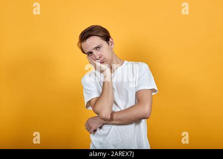 Der gutaussehende Mann in weißem T-Shirt sieht mit Kopf an Hand in die Kamera verzweifelt aus Stockfoto