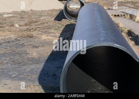 Prozess der Verlegung der Kanalisationsleitung. Runde Kunststoffröhrchen auf dem Hintergrund von ausgegrabenen Böden und Lehm Stockfoto